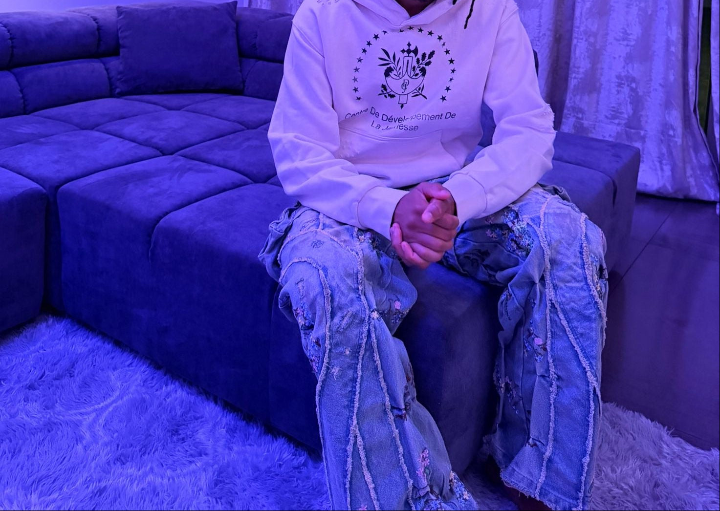 Michael Olise sitting on a couch in a room with blue lighting and white curtains.